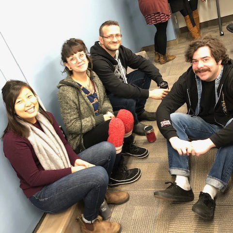 Jamie, Dom, Mike, Andrew sit on the floor at an all-staff meeting in 2019
