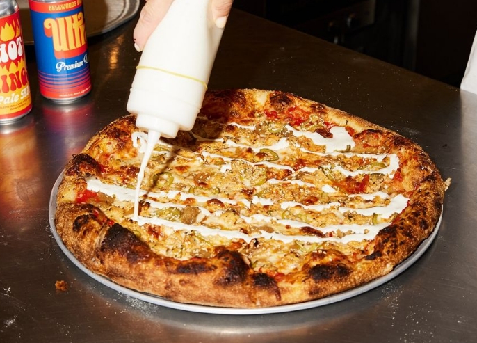 A hot and fresh pizza pie sits on a pan, a hand hovers, pouring on some ranch blue cheese dressing.

Une tarte à pizza chaude et fraîche est posée sur une poêle, une main plane, versant de la vinaigrette au fromage bleu et au ranch.